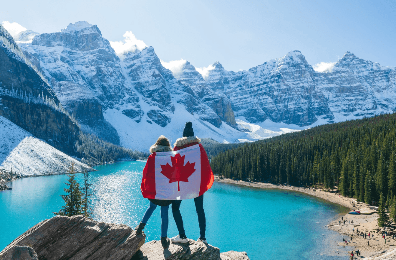Two people wrapped in a Canadian flag, looking out over a mountain lake